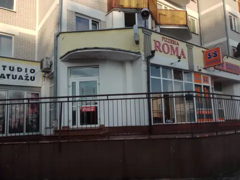 Parter budynku mieszkalnego, nad witryną czerwony napis PIZZERIA ROMA.